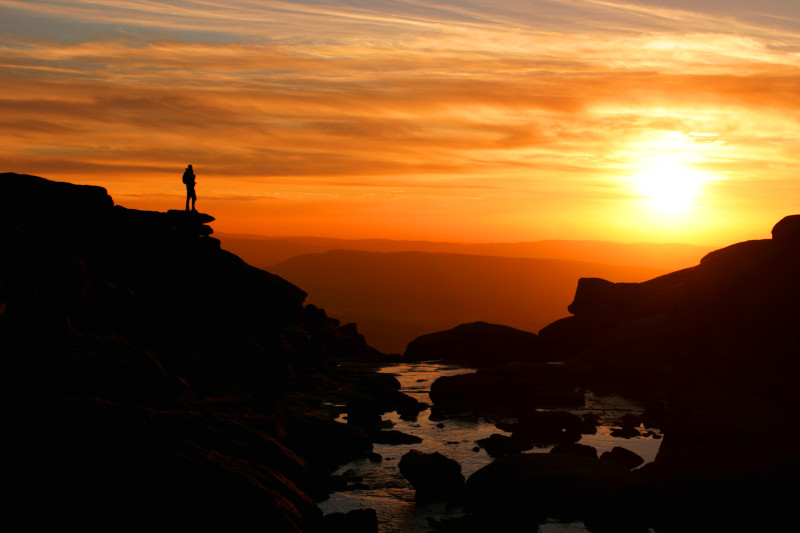 Sunset at Kinder Downfall with walker silhouetted against mountain backdrop