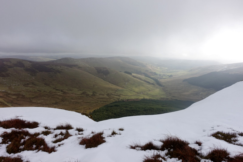 View east from snowy summit with forest and hills beyond